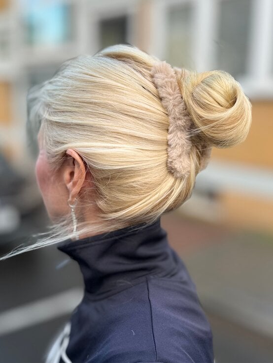 Blondhaarige Renate Zott mit elegantem Dutt und flauschigem Haarband blickt seitlich, trägt dunkle Jacke und funkelnden Ohrring. | © Renate Zott