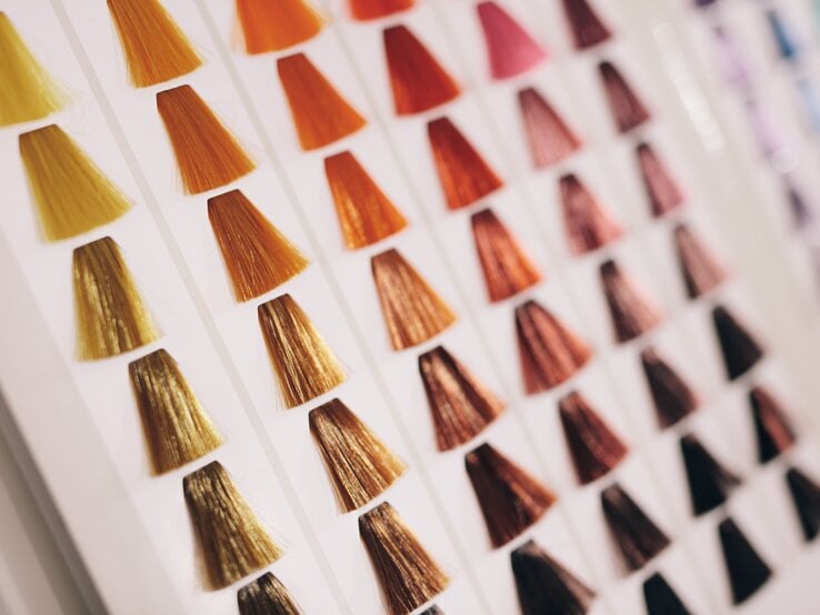 Fächer aus Haarfarbmustern in warmen Braun-, Kupfer- und Blondtönen auf weißem Karton, schräg fotografiert im Salonlicht.