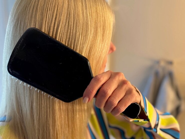 Renate Zott bürstet sich mit einer schwarzen Paddle-Brush die glatten Haare vor hellem Badezimmerhintergrund. | © Renate Zott