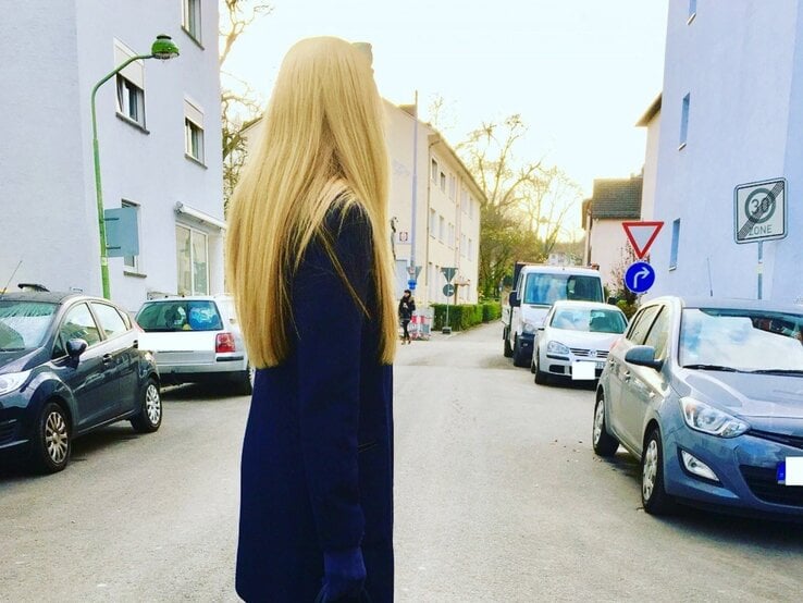 Renate Zott mit langem Haar und dunkelblauem Mantel steht nachdenklich in einer ruhigen Wohnstraße bei Abendlicht. | © Renate Zott