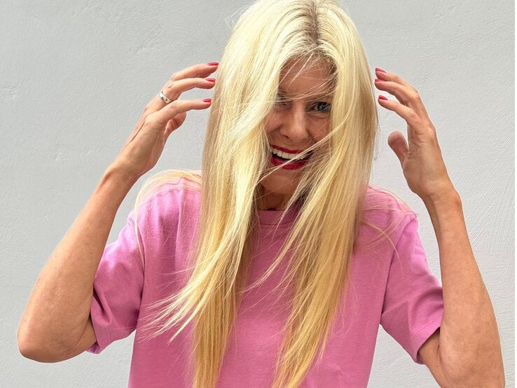 Lachende Renate Zott in pinkem Shirt streicht sich mit roten Fingernägeln die Haare aus dem Gesicht.