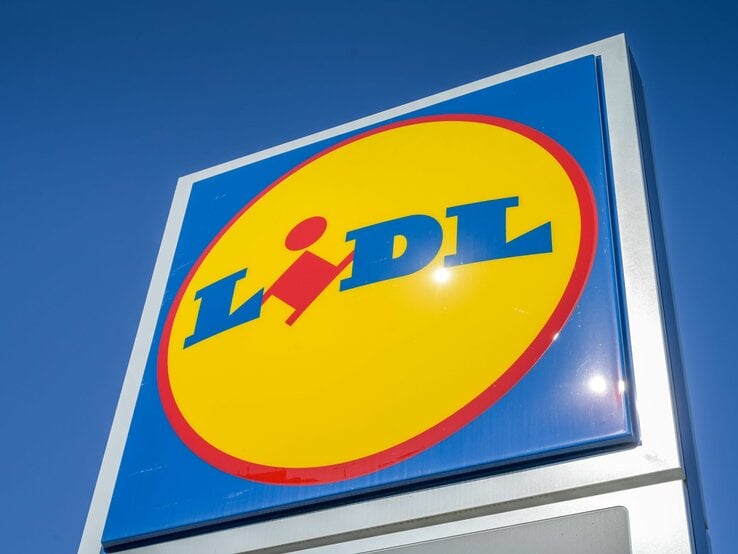 Sonnenstrahlen spiegeln sich auf einem scharf fokussierten Lidl-Logo unter blauem Himmel.
