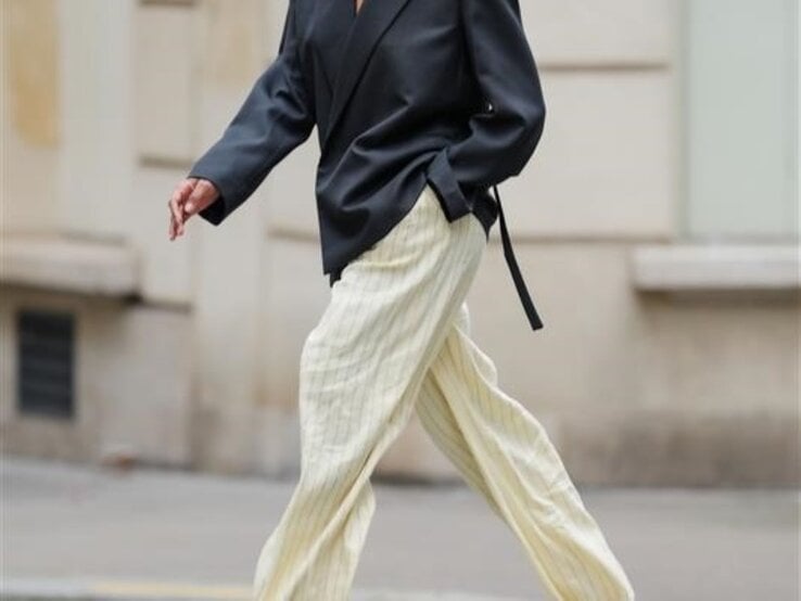 Zu sehen ist eine Frau, die eine Hose in Buttergelb und ein graues Oberteil trägt