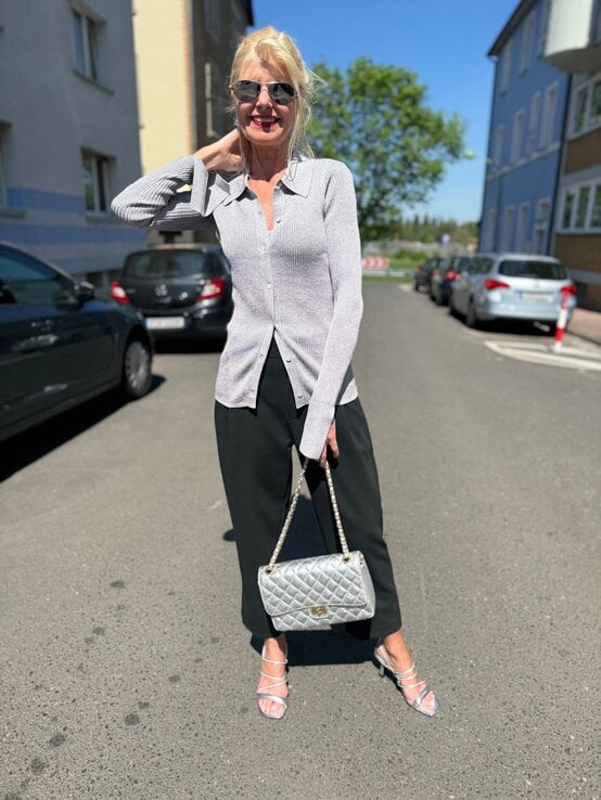Renate Zott mit blondem Dutt und rotem Lippenstift trägt silbernen Cardigan mit Polokragen, schwarze Culotte und silberne Sandalen. | © Renate Zott