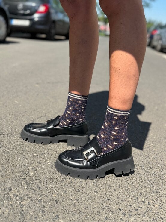 Schwarze Loafer mit grober Sohle und silberner Schnalle, kombiniert mit glitzernden Söckchen in Leo-Optik auf Asphalt. | © Renate Zott