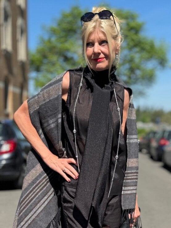 Renate Zott mit blondem Dutt trägt transparentes schwarzes Top mit schimmerndem Schal und Fransencape, blickt lächelnd zur Seite. | © Renate Zott