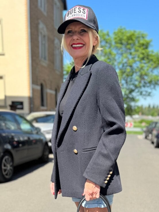 Renate Zott kombiniert schwarze Cap mit auffälligem Label und strukturierter Tweedjacke mit doppelter Knopfreihe. | © Renate Zott