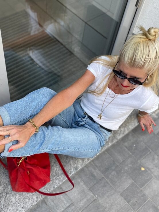 Blondierte Renate Zott mit Dutt posiert lässig auf einer Fensterbank, trägt rote Heels mit Nieten, Jeans und weißes T-Shirt. | © Renate Zott 