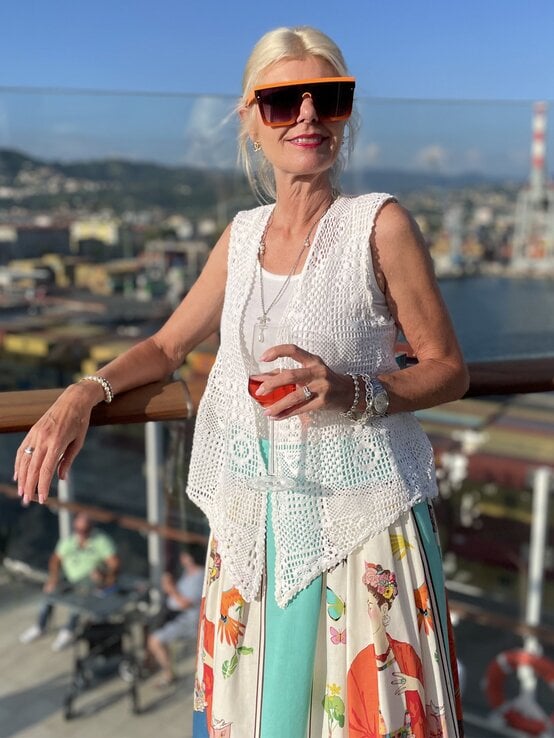 Renate Zott mit extragroßer Sonnenbrille und Häkelweste hält ein Glas Aperitif auf einem sonnigen Kreuzfahrtschiff. | © Renate Zott 