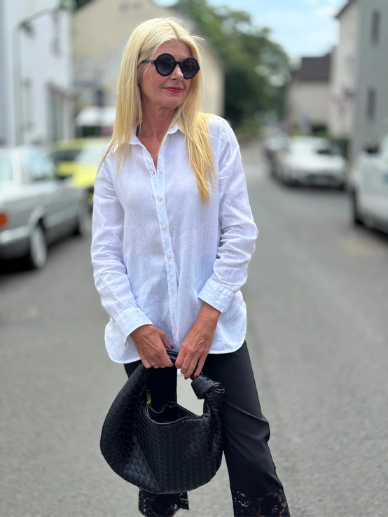Blondierte Frau mit schwarzer Sonnenbrille, weißer Bluse und Spitzendetails an der Hose hält eine geflochtene schwarze Handtasche. | © Renate Zott