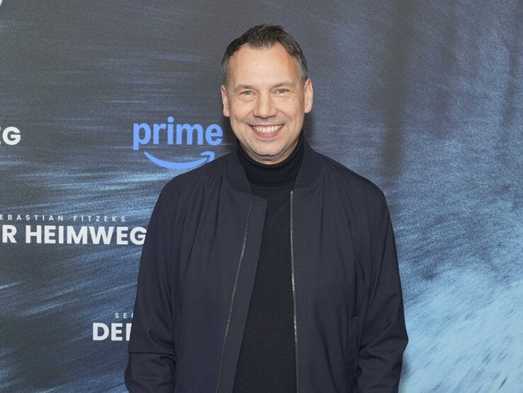Sebastian Fitzek in dunkelblauer Jacke und schwarzem Rollkragenpullover steht vor einer Fotowand mit Schriftzug und Prime-Logo.