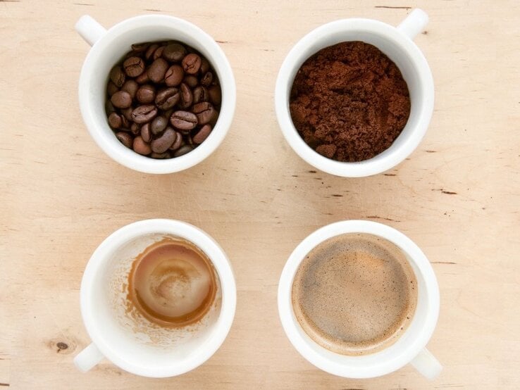 Vier weiße Tassen zeigen Bohnen, Pulver, frischen Kaffee und Kaffeereste als Phasen der Kaffeezubereitung von oben.