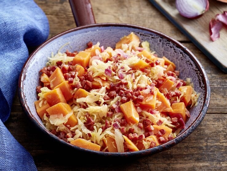 Süßkartoffel-Sauerkraut-Pfanne auf hölzernem Hintergrund. Links davon ein blaues Geschirrtuch.
