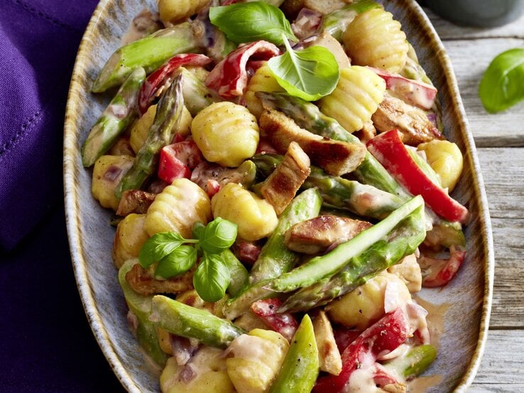 Gnocchi-Schnitzel-Pfanne auf einem großen Teller auf hölzernem Hintergrund. Links davon ein blaues Geschirrtuch.