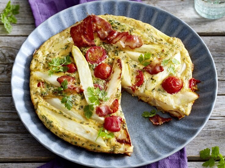 Spargel-Frittata auf einem blauen Teller auf hölzernem Hintergrund. 