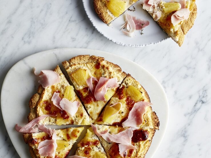 Zwei weiße Teller mit der Low-Carb-Pizza auf hellem Marmoruntergrund direkt von oben fotografiert