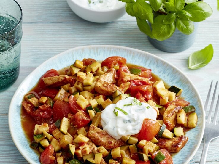 Steak-Streifen mit Tomaten-Zucchini-Ragout und frischem Kräuterquark angerichtet auf hellem Holz mit Basilikumdeko.
