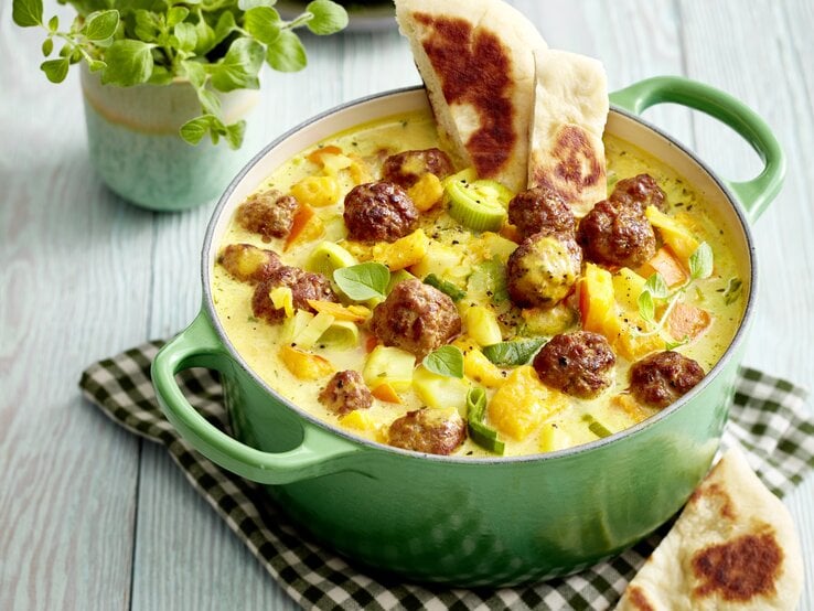 Hackbällchen-Kürbis-Eintopf mit zwei Stücken Brot in einem grünen Emaille-Topf, der auf einem Küchentuch steht, schräg von oben fotografiert