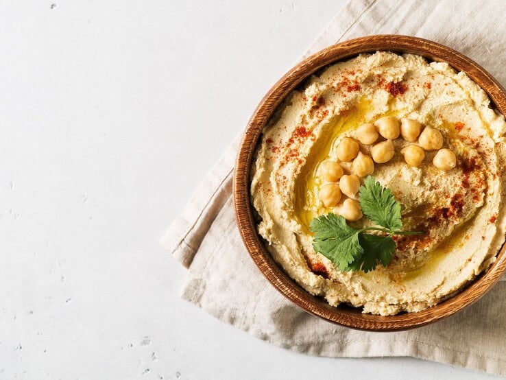 Klassischer Hummus und ganze Kichererbsen in einer runden Schüssel aus Ton / Handtuch / Draufsicht
