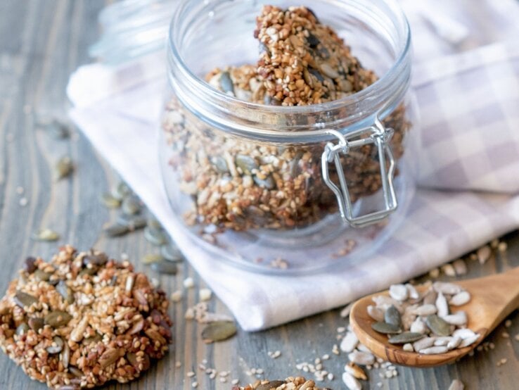 Low Carb Cracker mit Kernen in einem Schraubglas, daneben einige Cracker und verstreute Kerne auf einem Holztisch.