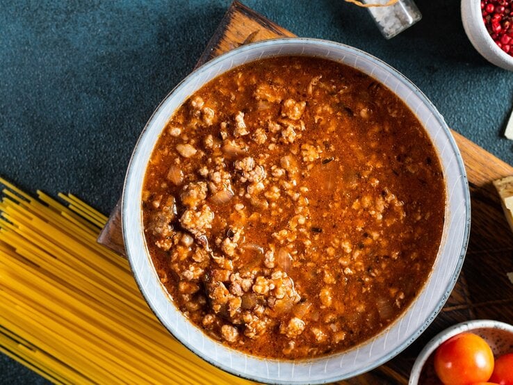 Haschee im runden Topf / ungekochte Spaghetti / Frische Tomaten in runder Schüssel / Draufsicht
