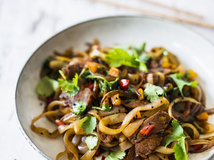 High Protein Nudeln mit Schweinefilet und Paprika in einer weißen Prozellanschüssel vor weißen Hintergrund.