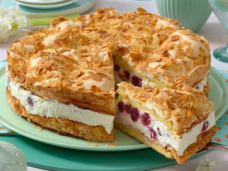 Himmelstorte mit Cremefüllung und gerösteten Mandelblättern obenauf / auf rundem Teller aus Porzellan / Frontalsicht